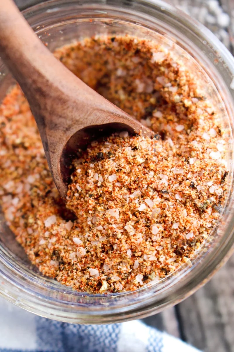 Closeup of brisket dry rub in a small glass jar with a wood spoon in it.