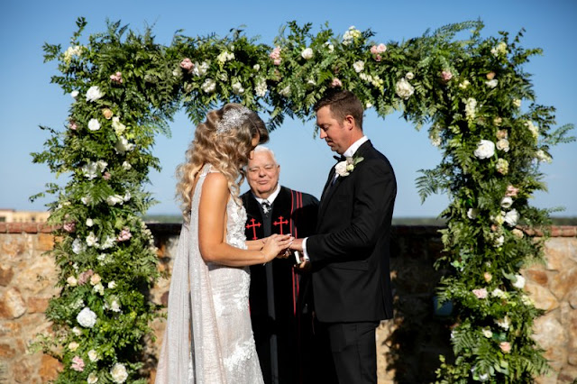 bride and groom holding hands in front of greenery arch at wedding ceremony
