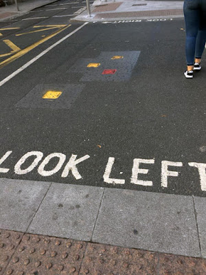 A crosswalk on asphalt, with 'look left' printed large on the near side, and 'look right' with an arrow printed on the far side.