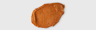 A large oval orange splurge of face mask with bits of grounded light brown seeds in on a white background