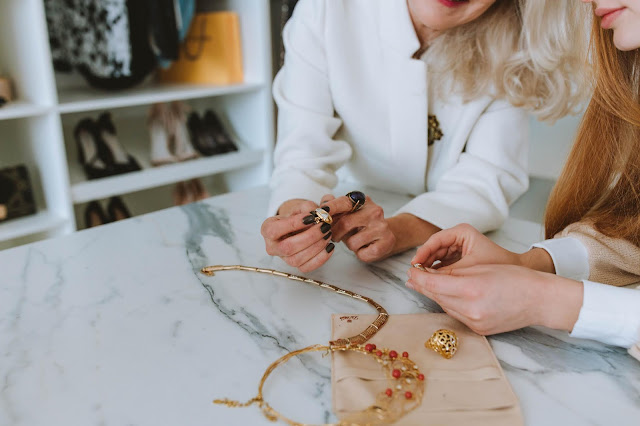 Two women admiring jewelry on a marble table.