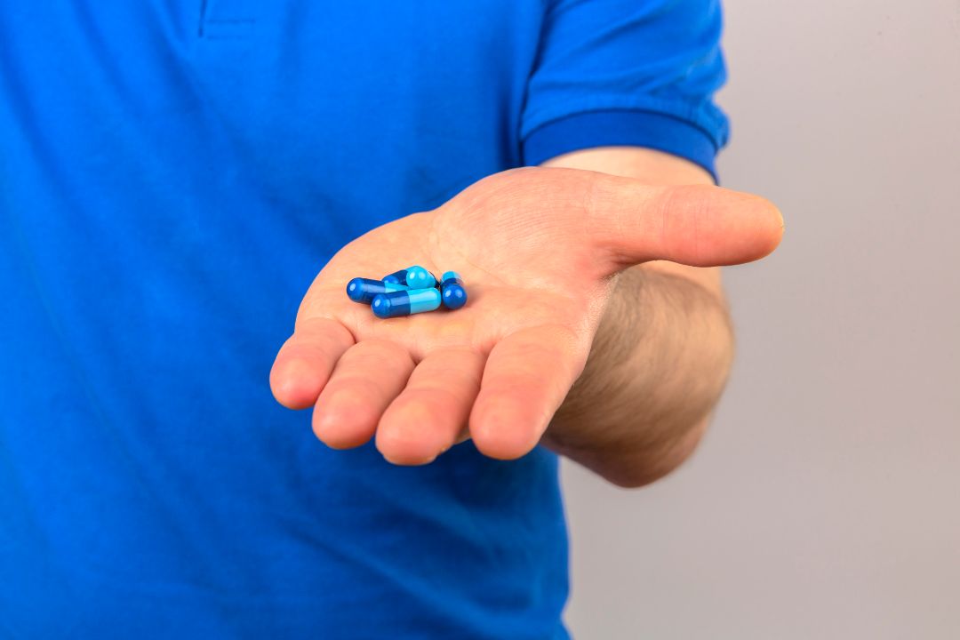 Man in blue scrubs offering pills from hand