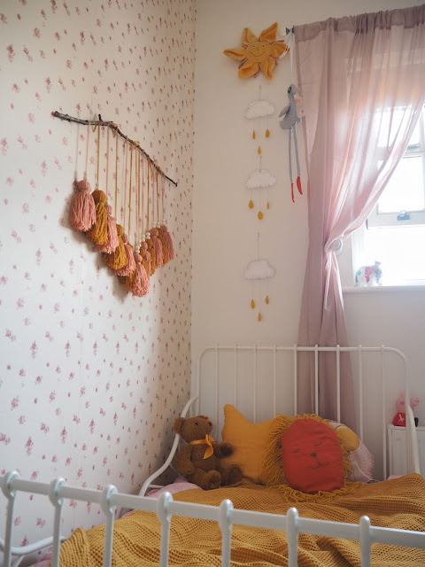 A pink and mustard yellow girls nursery bedroom, complete with cute accessories, colourful decor and homemade DIY touches. Including the IKEA Minnen bed, boho wall hanging, and IKEA hack dollhouse. Nursery inspiration and budget ideas.