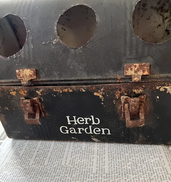 Photo of a vintage lunch box with three holes and herb garden stenciled on it.