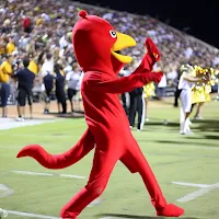A person dressed as a chili pepper mascot dancing at a VCSpreps football game.