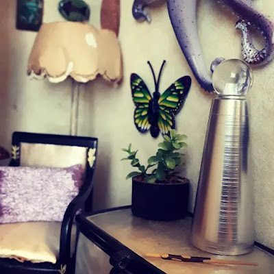 Corner of a one-twelfth scale witch's study with a reading chair and lamp, and a chest with a modern crystal ball and wand on it.