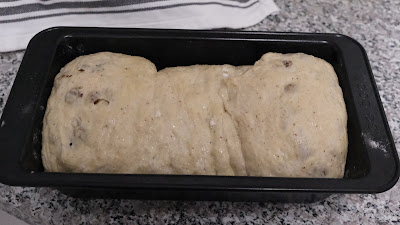 Sultana bread dough in a black loaf tin