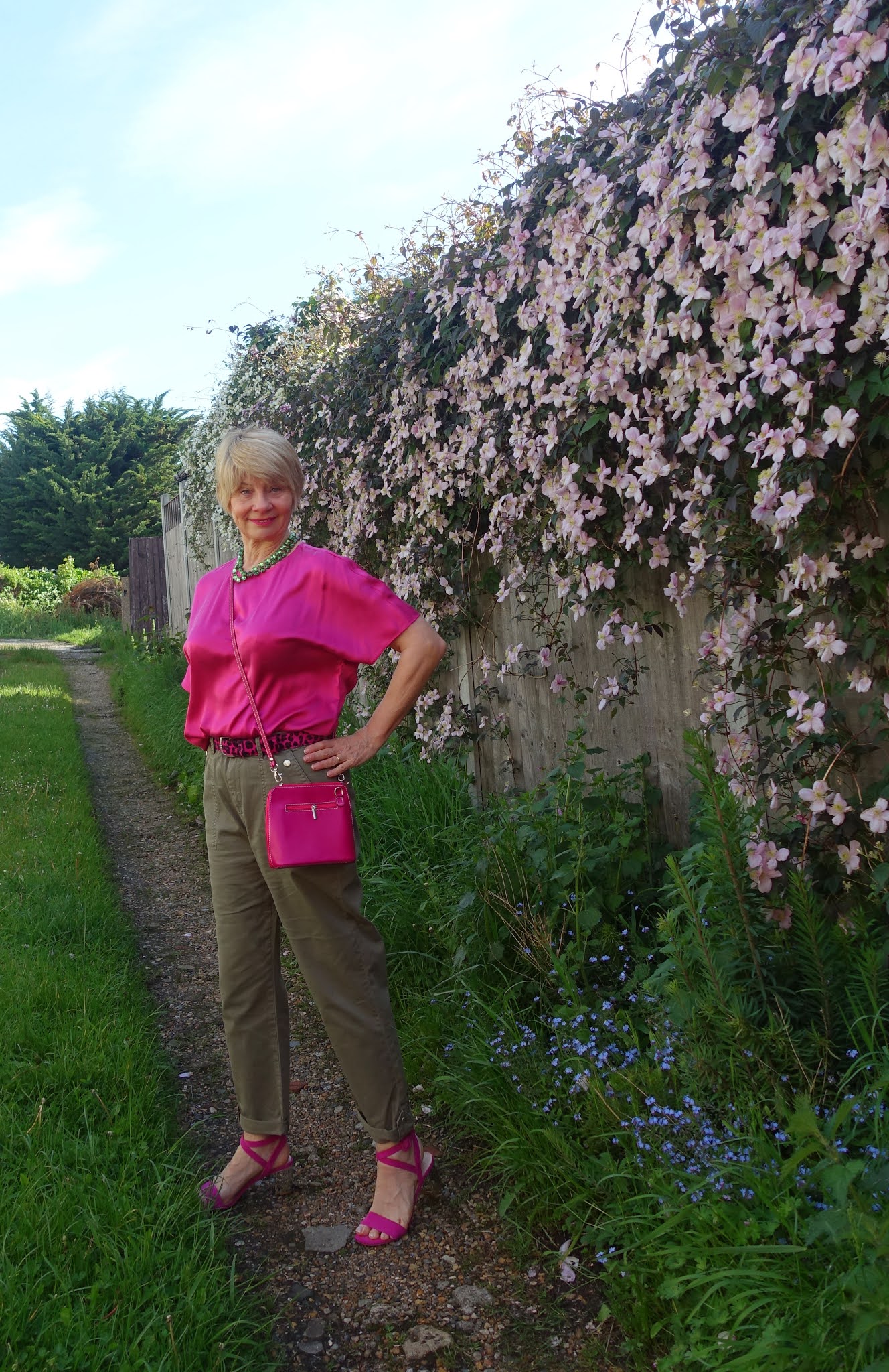 Over 50s blogger Gail Hanlon in khaki cargo trousers and bright pink silk blouse against a clematis montana backdrop