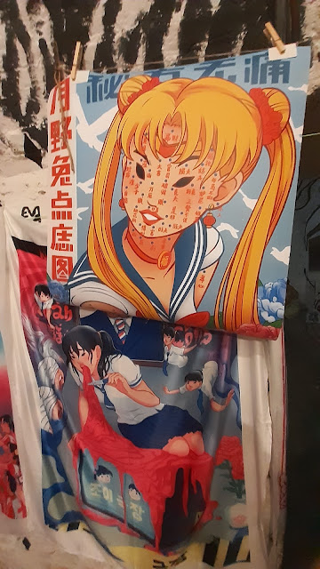le magliette e le illustrazioni dell'artista: qui una Sailor Moon e una donna in un'uniforme da scuola che vomita