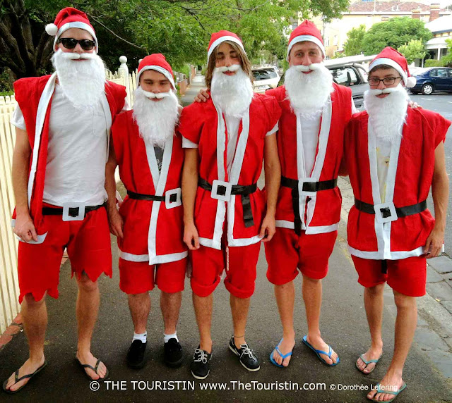 Five young men dressed up as Santa Claus with short red bermudas and flip flops.