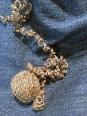 A small ball of grey yarn, with a very crimpy tail trailing off across the blue denim background.