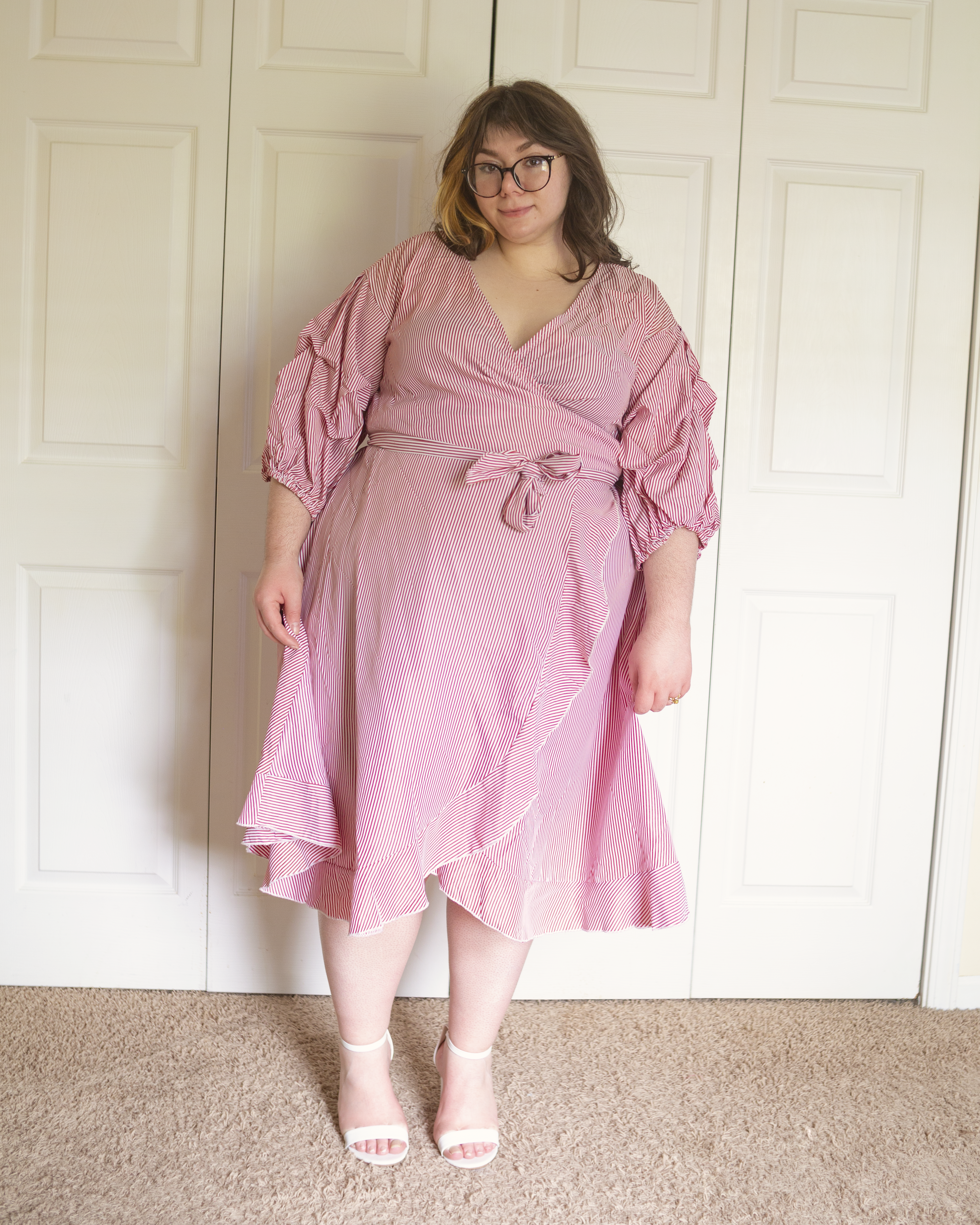 An outfit consisting of a pink pinstripe on white puffy sleeve midi wrap dress with white ankle strap heeled sandals.