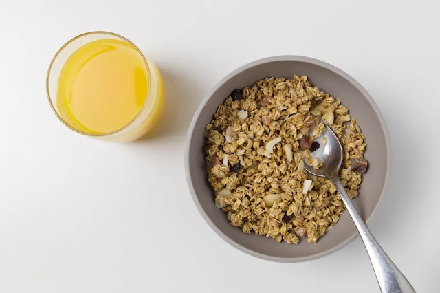 Plato con granola y vaso con jugo de naranja. Tips para bajar de peso.