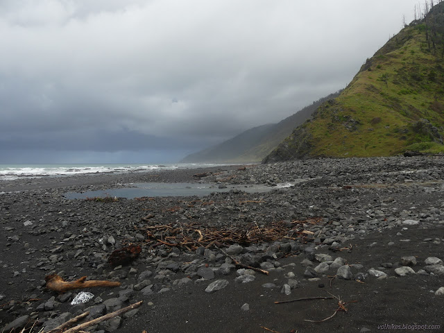 100: rocky beach and green hills and rain over ocean