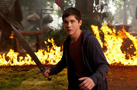 Logan Lerman caracterizado de Percy Jackson en una imagen oficial de la película El Mar de los Monstruos. Vemos a Percy con Riptide en alto y con una barrera de fuego detrás.