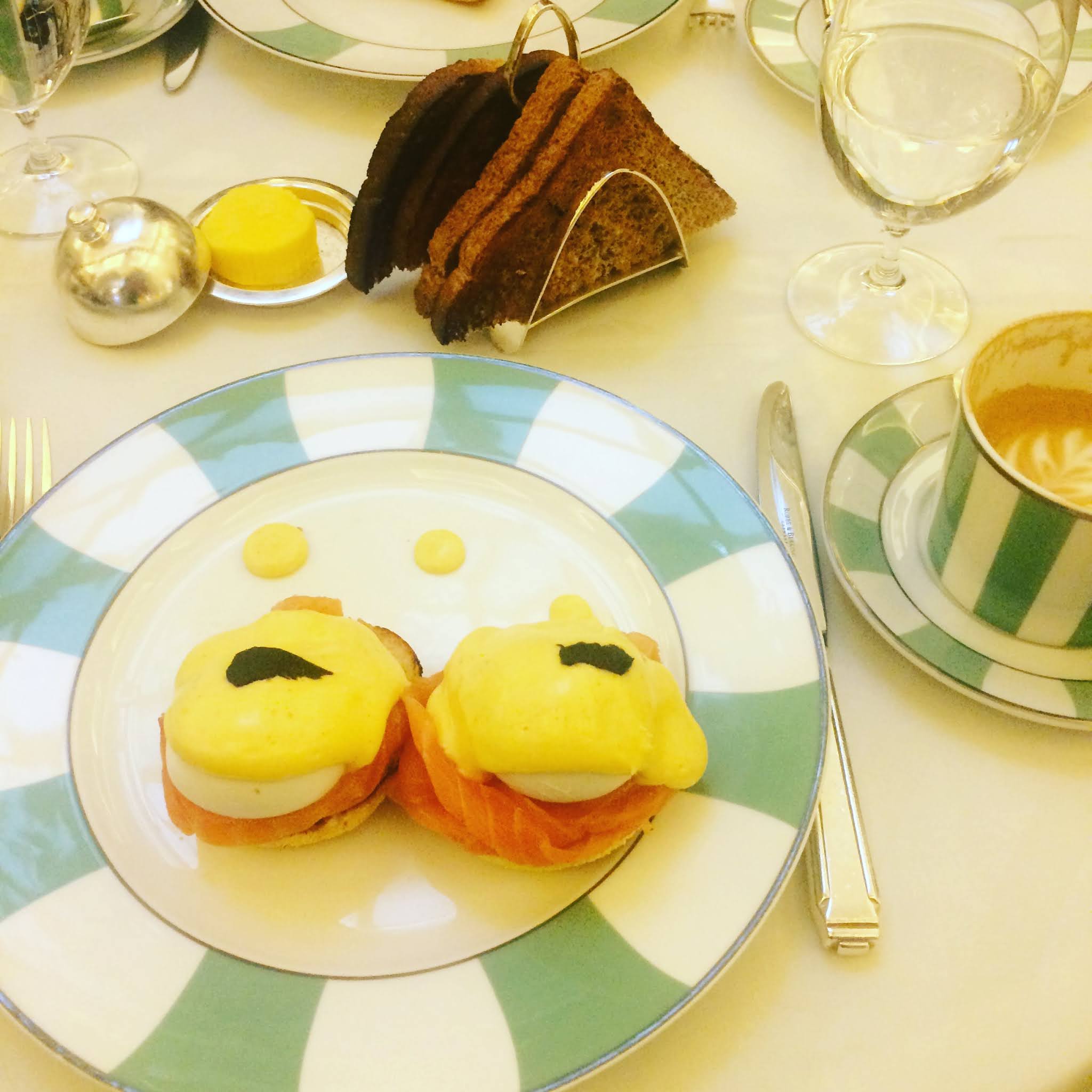 A white and blue plate of eggs royale next to burnt toast at Claridge's, one place to avoide for breakfast in london