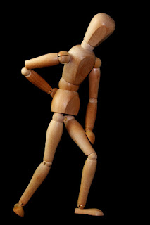 Wooden doll leaning forward with hand on back - Image by Wolfgang Claussen from Pixabay