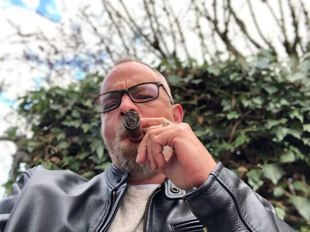 1/3 Man in his late 40s smoking a cigar wearing a black leather jacket is glasses on