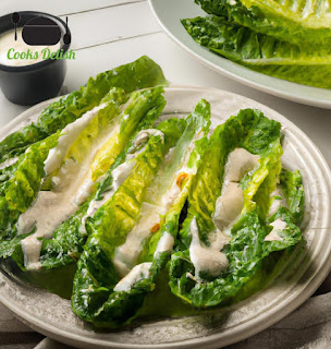 A fork cutting through a piece of grilled romaine lettuce with Caesar dressing on top