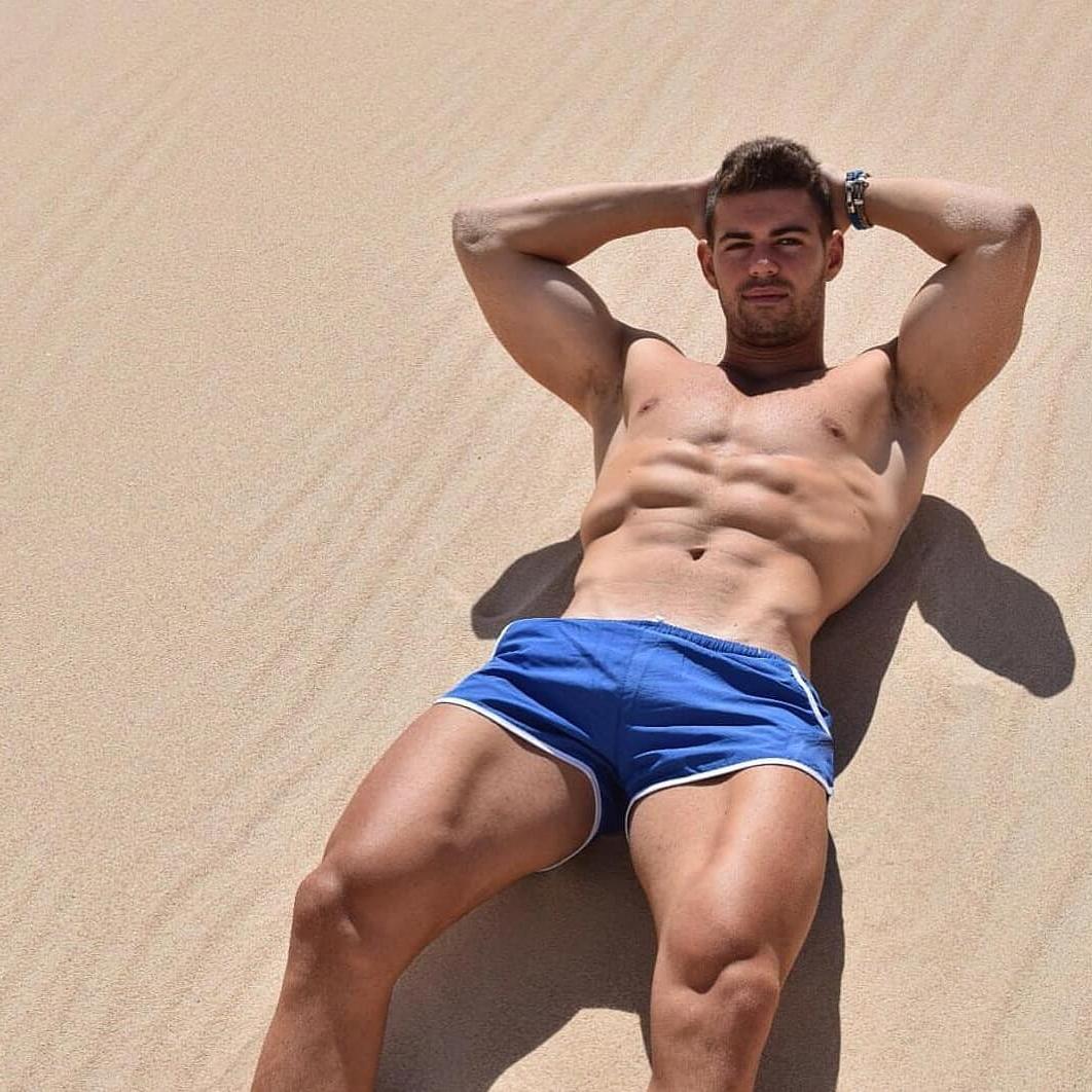 hot-shirtless-guy-muscles-laying-sand-blue-shorts