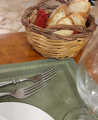 Tavola apparecchiata elegantemente in una masseria pugliese con un cestino di pane fatto con un vimini intrecciato.