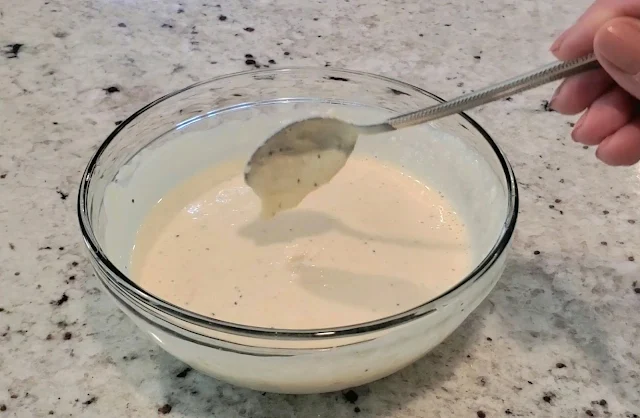 A bowl of Caesar salad dressing being stirred with a spoon.