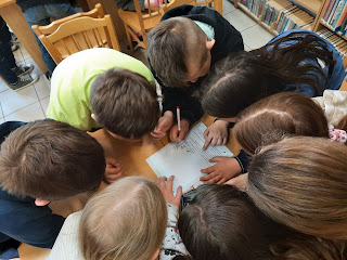 Na zdjęciu grupa dzieci rozwiązująca zadanie na kartce papieru.