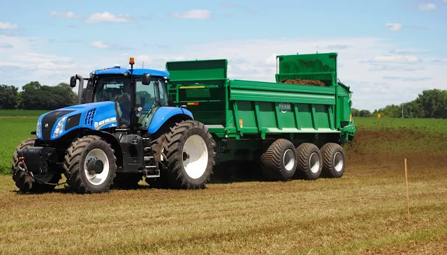 Blue tractor applying manure with a manure spreader in a field on a sunny day