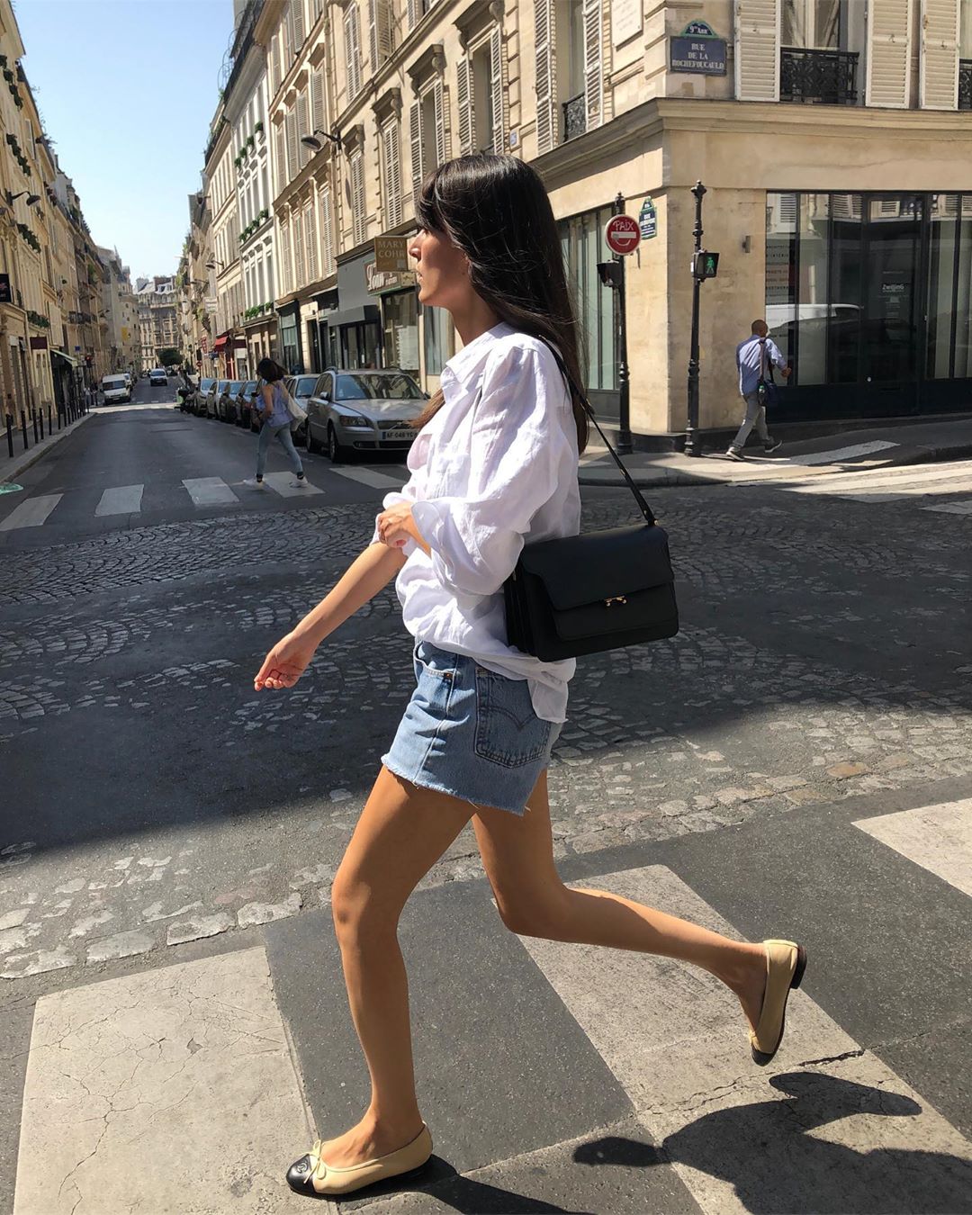 The French Girl Way to Wear Cut-Off Denim Shorts — Leia Sfez summer oufti idea with jean shorts, a classic white button-down shirt, classic black shoulder bag, and Chanel cap-toe flats