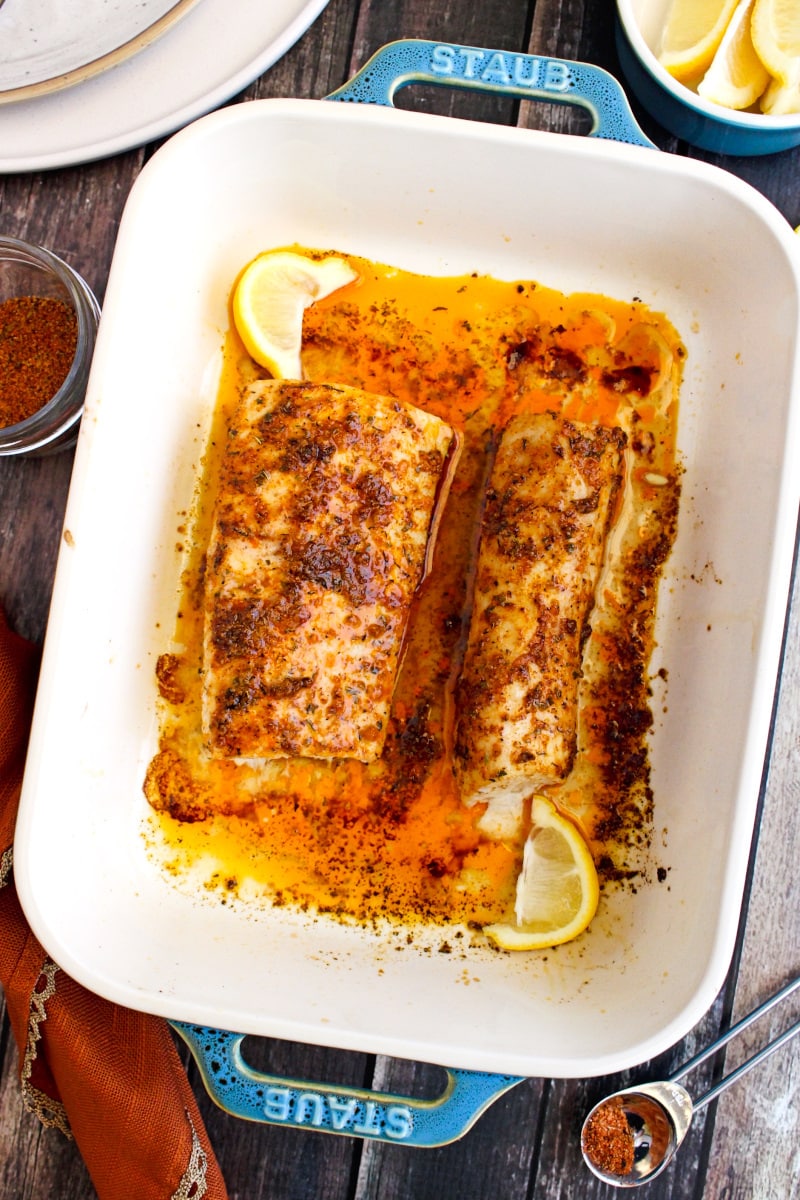 Cajun Baked Mahi Mahi in a cream baking dish with teal handles with lemon wedges and an orange napkin sitting next to it.