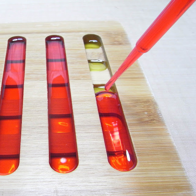 Using a pipette to transfer coloured resin into the slots of a bamboo trivet.