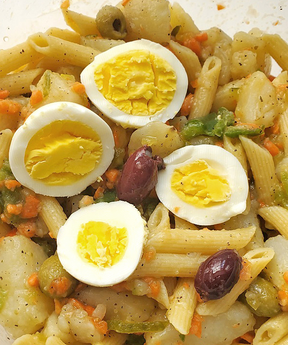 pasta and potato salad with boiled eggs and vegetables in a bowl with olives and vegetables