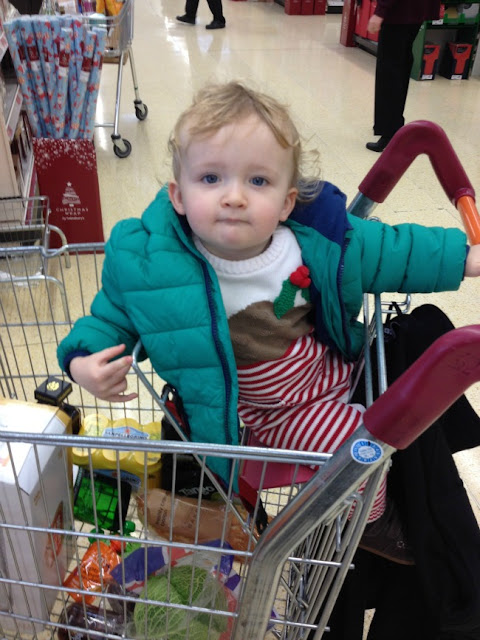 Toddler sat in shopping trolley wearing Christmas pudding suit