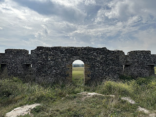 A view from inside the Arx Ruochim folly showing a circular stone base where the tower once stood.  In the background the door of the folly gives a view out onto a grassy area.  Photo by Kevin Nosferatu for the Skulferatu Project.