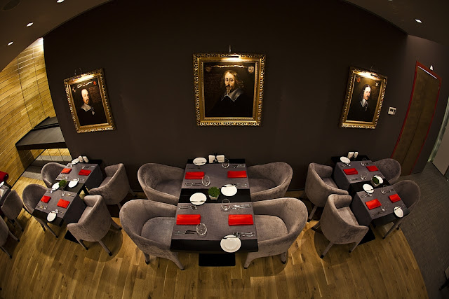 Picture of square dining tables with grey velvet chairs by the dark brown wall