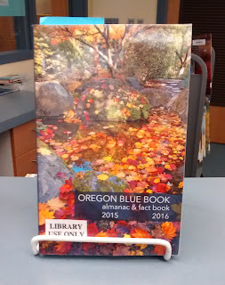 Oregon Blue Book almanac and fact book for 2015-2016, standing upright in a wire stand on a library counter