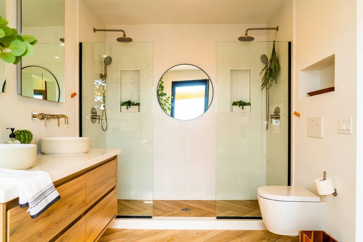 Baño con doble ducha al fondo, con dos  mamparas fijas y dos puntos de agua, con un espejo en el centro.