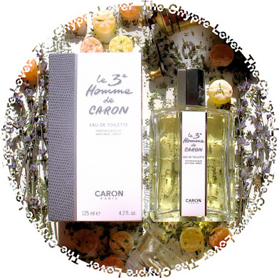 The bottle and cardboard box of Le 3e Homme de Caron by Caron (eau de toilette) lying flat amongst hard candies, lavender and dried tarragon leaves
