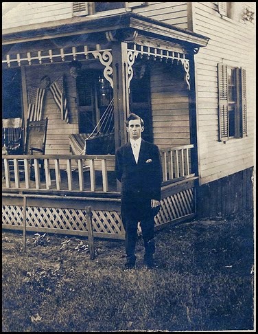 Gould_Harry in front of house with porch and flags_circa 1912