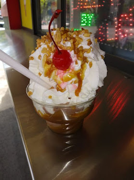 sundae in a clear dish, loaded with whipped cream, nuts, a cherry, and drizzle of caramel sauce