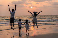 Una familia con dos hijos corre y salta mirando al mar en la puesta de sol.