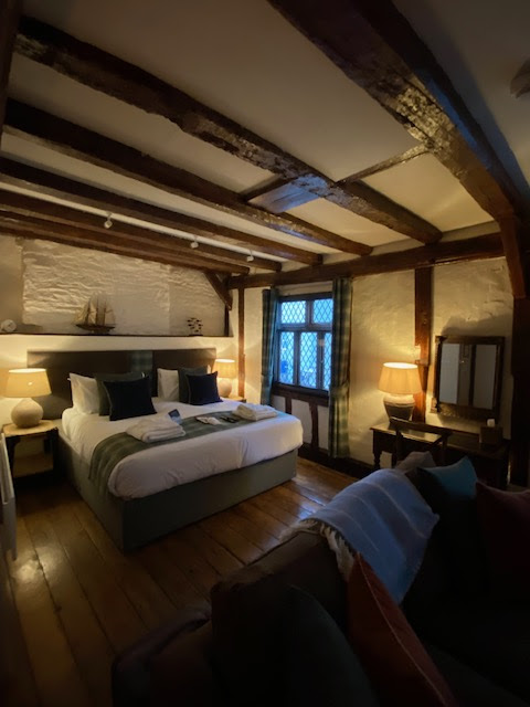 A bedroom in an old inn. The windows are leaded, and the sloping ceiling supported by thick dark beams.