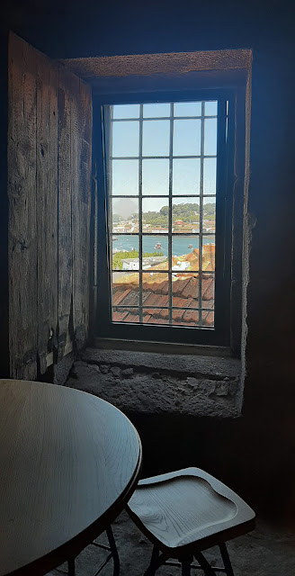 mesa redonda em frente à uma janela rústica de granito e madeira com vista para o Porto