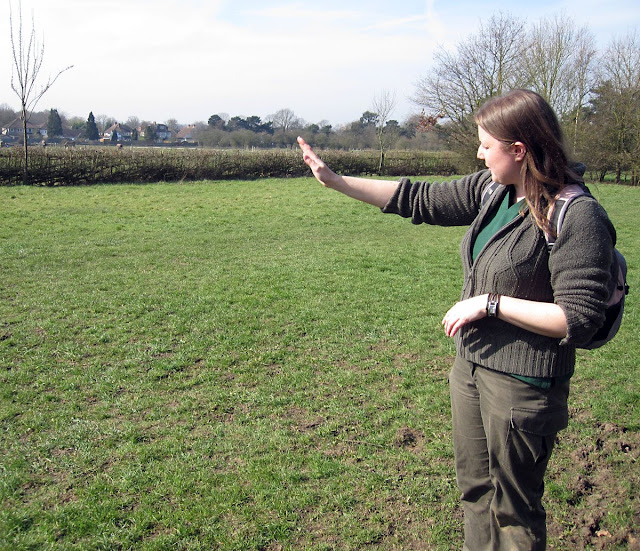 Jenny Price of BCS gesturing towards a pleached hedge across the meadow in Jubilee Country Park