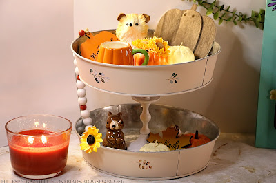 Tiered tray decoration displaying fall decorations with lit candle beside it