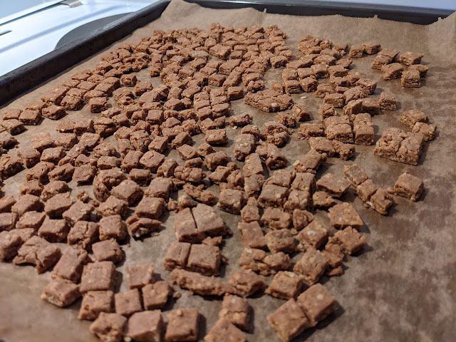 Peanut butter dog biscuits, baked, on a baking sheet lined with parchment paper. The shapes are small squares.