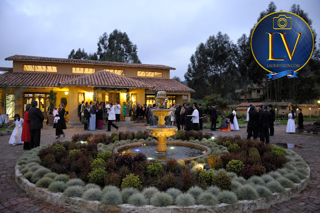 fuente al atardecer detrás la hacienda con luces amarillas y arboles