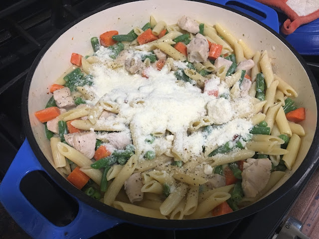 Grated parmesan being added to the creamy chicken and vegetable pasta.