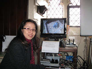 Jennie Mak inside the ringing-chamber of Derby Cathedral with a female peregrine visible in the monitor behind her