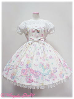 The toy parade one piece dress. It is the white colourway and has a big bow in the centre. It has short puff sleeves and a Peter-pan collar. There is lace along the bottom of the skirt.